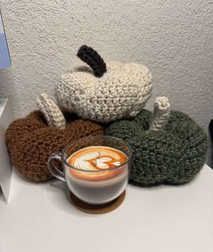 Crochet pumpkins next to a cup of coffee on a textured surface