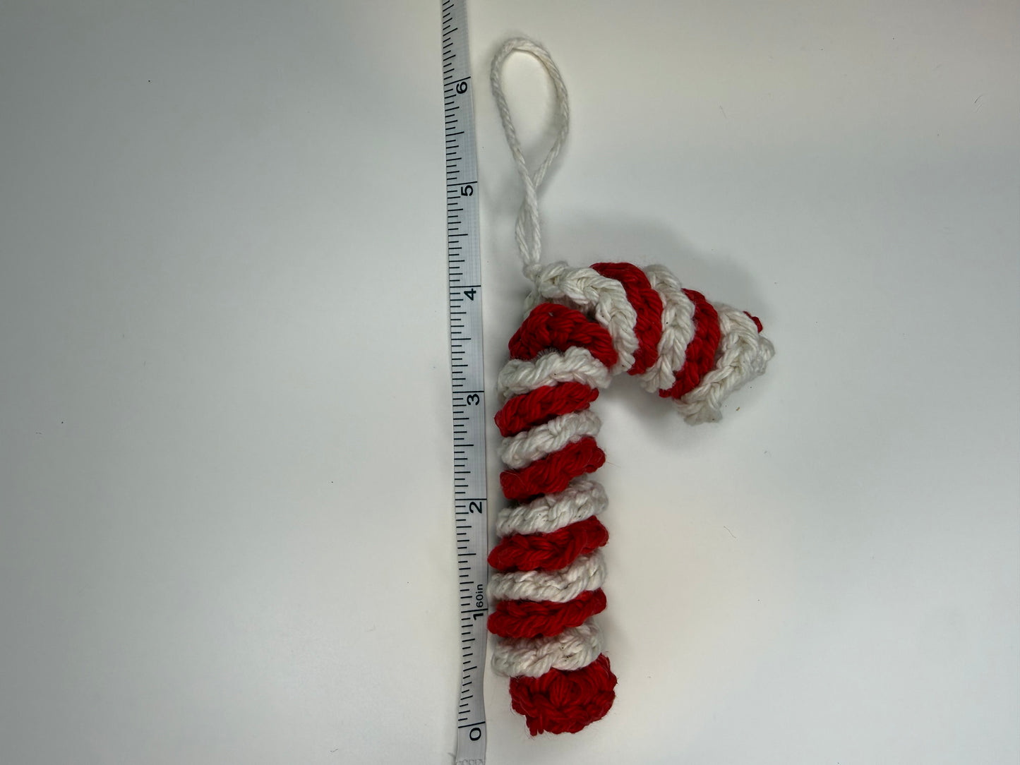 Crocheted candy cane ornament next to a ruler on a white background