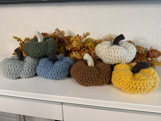 Set of crocheted pumpkins in various colors on a white surface with autumn leaves.