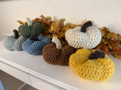 Crochet pumpkins in various colors on a white surface with autumn leaves.