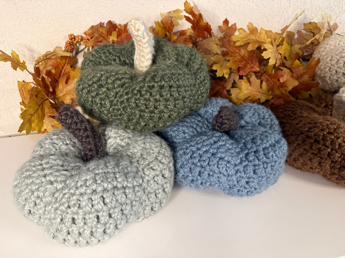 Crochet pumpkins in various colors on a white background with autumn leaves.