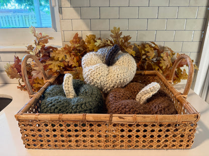 Wicker basket with crochet pumpkins and leaves on a kitchen counter.